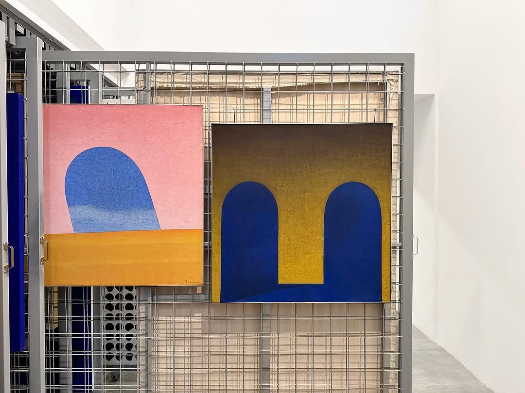 Duas pinturas geométricas expostas sobre grade metálica